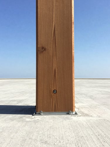 Close-up portrait shot of a heavy timber deck post anchored to a concrete footing with robust fasteners, crisp shadows, bright sunlight, wide-angle view from below.