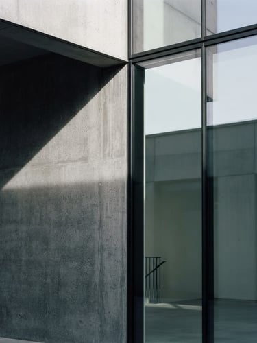 Minimalist architectural corner of a concrete and glass structure, sharp geometric shadows, soft north-facing daylight, high contrast slate tones, 35mm