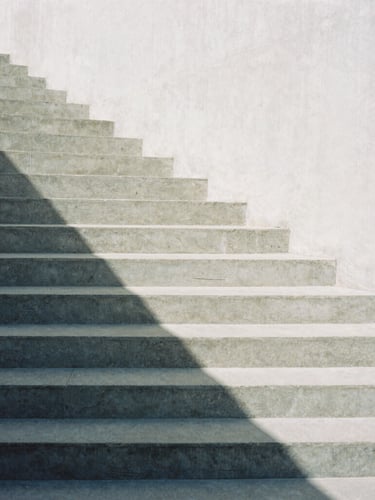 Minimalist architectural photography of a concrete staircase casting sharp geometric shadows under soft daylight, high contrast slate and white tones, 35mm