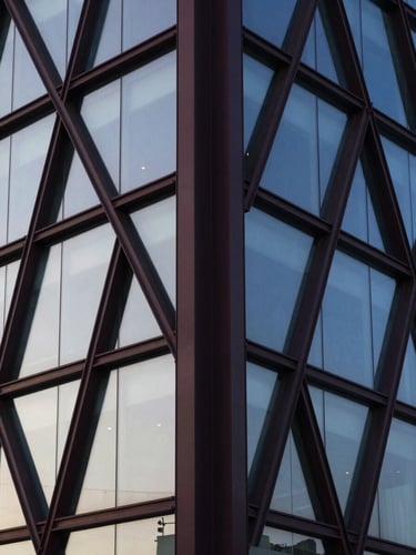 Abstract structural geometry of a modern architectural facade, sharp angles of steel and glass reflecting a clear morning sky, deep navy tones, high-contrast
