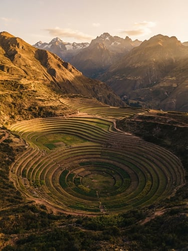 Vista aérea de terrazas agrícolas en el Valle Sagrado, rodeadas de imponentes montañas andinas bajo una luz dorada de atardecer, estilo editorial, formato medio.