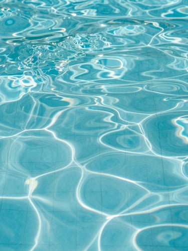 Macro shot of crystal-clear turquoise water rippling gently in a pool, clean geometric tile lines visible below, bright midday sunlight
