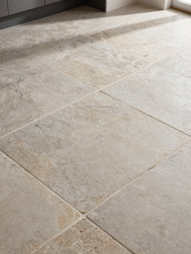 Angled overhead shot of floor tiles and natural stone pavers in a renovated kitchen, grout lines clean and visible, morning light revealing texture and finish variation