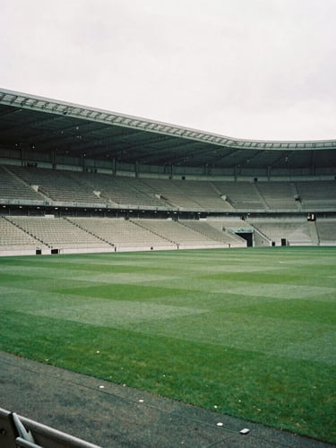 A wide architectural angle of an empty historic stadium in soft morning light, overcast British daylight, muted forest green and slate tones, editorial film photography style, 35mm lens.