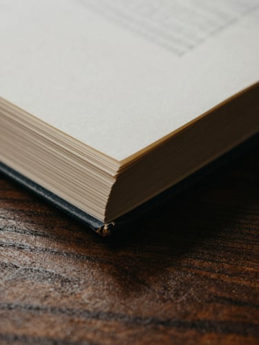 A close-up macro shot of deckled book edges and heavy paper stock resting on a dark wooden table, soft indirect daylight casting quiet shadows, warm editorial tones.