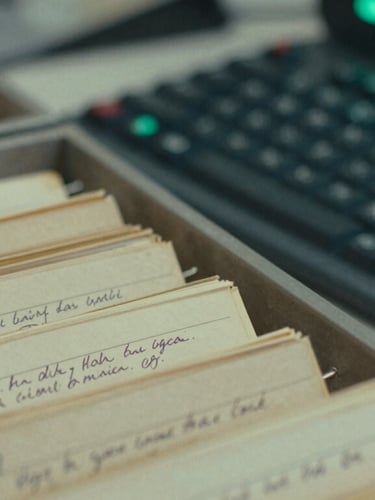 Macro close-up of a vintage library catalog card drawer with hand-written index cards next to a modern mechanical keyboard with a glowing green LED screen in the background, cool fluorescent lighting