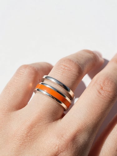 Macro shot of a hand wearing three stacked silver and orange enamel rings, bright natural daylight, crisp white background, 35mm lens.