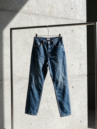 Stark fashion photography, a heavy raw denim garment hanging on a raw steel rack, high-contrast side-lighting, concrete background, 35mm