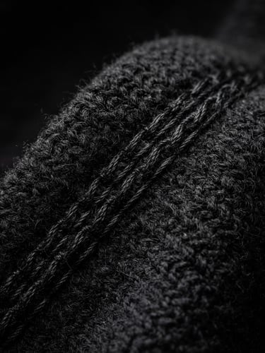 Extreme close-up on heavy black cotton knit fabric, showing rich texture and clean double-needle stitching, dramatic high-contrast studio lighting, deep shadows, 85mm lens