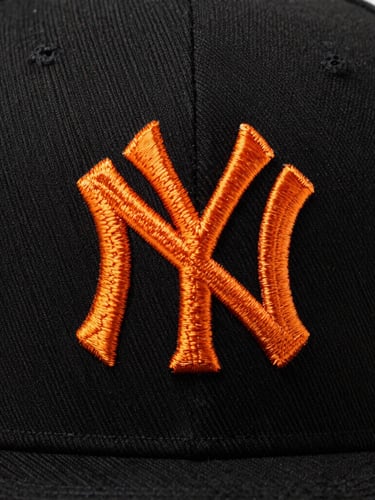 Extreme macro shot of a black snapback cap with detailed orange embroidery, high-contrast studio lighting, sharp thread textures, 85mm lens