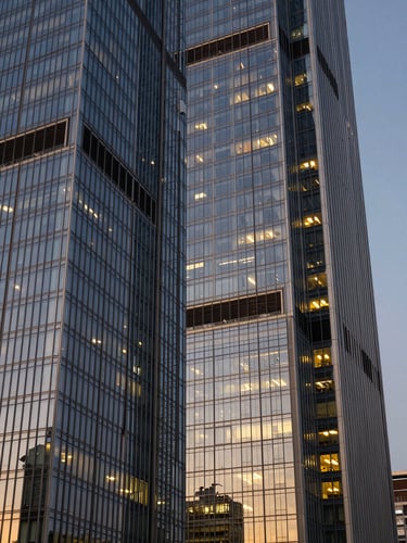 Dramatic twilight shot of modern glass skyscraper facades reflecting golden lights, sharp angles, clean luxury architectural framing.