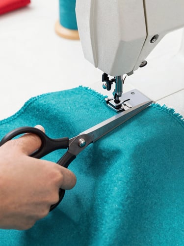 Close-up of hands cutting vibrant teal fabric with tailoring scissors, sewing machine in a bright sunlit Celaya workshop, detailed texture of high-quality textiles.