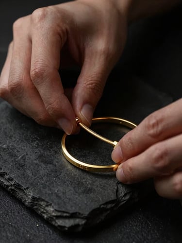 Elegant hands carefully inspecting a gold bracelet on a dark textured stone, dramatic low-key lighting, deep black and gold tones, macro lens, shallow depth of field.
