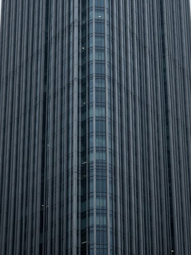 Minimalist architectural crop of high-end corporate skyscraper corner, sharp geometric lines against cool overcast daylight, desaturated blue and charcoal tones.