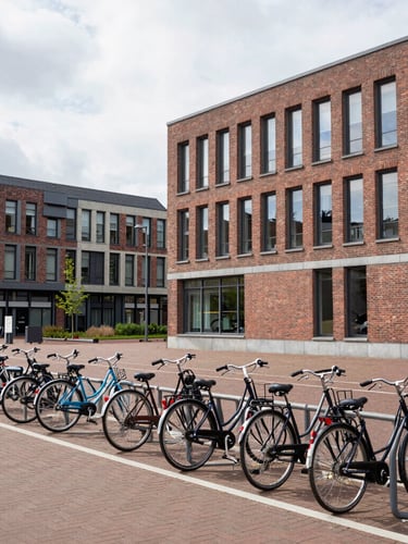 Wide environmental shot of a modern brick university campus in Utrecht with bicycle racks in the foreground, bright overcast northern European daylight, clean architectural lines.