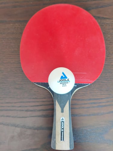 Análise de aderência e cabo ergonómico de madeira em raquete de ténis de mesa Joola com bola.