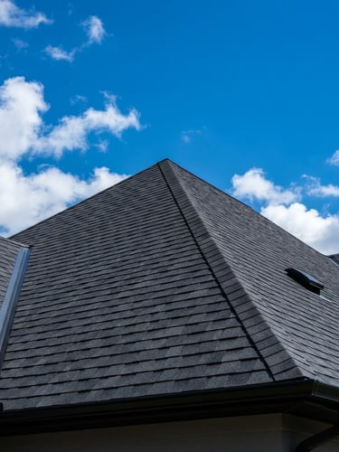Low-angle architectural shot of a secure, newly shingled roofline against a bright blue sky, daylight emphasizing clean shingle alignment, 35mm