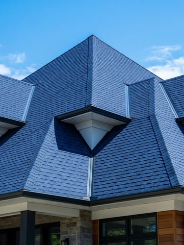 Low-angle architectural shot of a modern residential roof with immaculate dark blue shingles, sharp precision alignment, bright direct daylight highlighting texture.