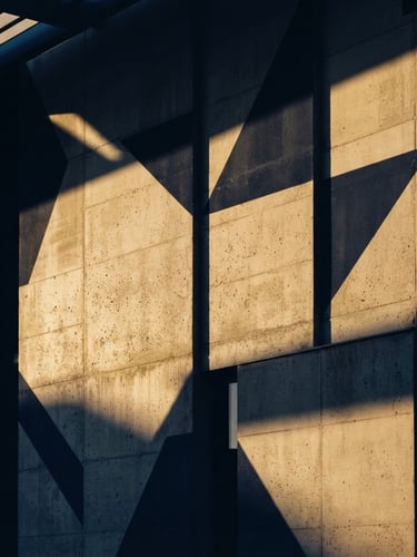 Minimalist architectural concrete facade with sharp geometric shadows cast by warm golden-hour sunlight, 35mm lens, high-contrast, deep navy tones