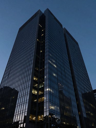 Wide architectural shot of a modern corporate skyscraper facade in São Paulo, sharp geometric glass angles reflecting a deep blue twilight sky, dramatic high-contrast shadows, low-key cool tones with subtle warm office lights glowing from within.