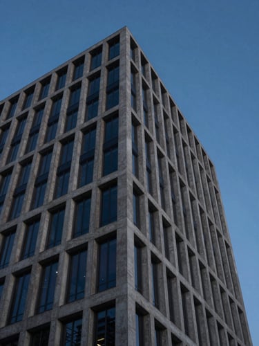 Sober architectural view of a modern financial tower corner, sharp concrete lines cutting into a deep blue dusk sky, low-key lighting.