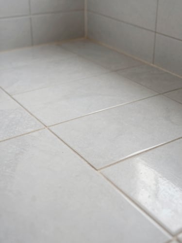 Close-up of a freshly tiled bathroom floor in a Turin apartment — precise grout lines, clean edges, porcelain tiles under natural daylight, no people, documentary quality proof of finish