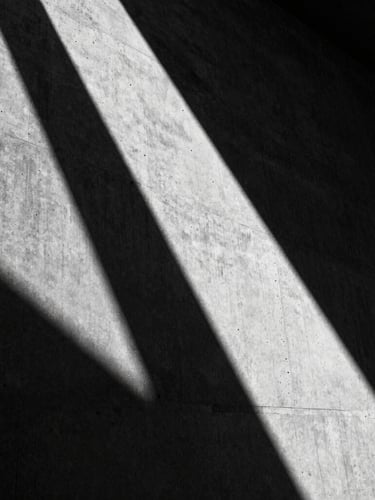 Extreme close-up of harsh low-angle sunlight grazing raw concrete, casting a deep diagonal shadow, 35mm architectural photography, high-contrast monochrome