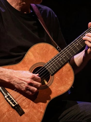 Close-up of hands playing a traditional Argentine acoustic guitar under high-contrast warm stage spotlights, rich copper tones and deep shadows, cinematic 35mm photography.