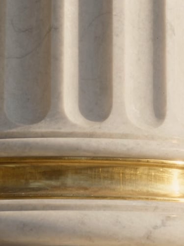 Extreme close-up of a premium white marble column with brushed brass inlay, warm golden hour light reflecting off the metallic edge, sharp architectural focus, 35mm.
