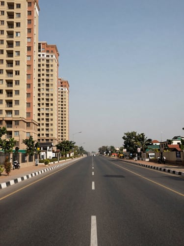 Ground-level architectural shot of a wide arterial road in Faridabad Sector 89 at midday—empty six-lane road surface fills the foreground, high-rise residential building façade visible on the left edge, clear blue-grey sky above, shot with a documentary wide angle, no people, no vehicles, structural precision framing