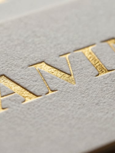 Macro shot of embossed business cards showing heavy linen texture and gold foil lettering, soft diffused side lighting.