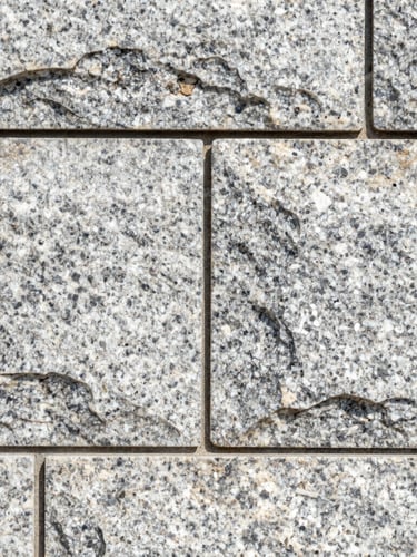 Close-up macro shot of perfectly aligned stone joints on a newly completed granite retaining wall, bright morning daylight, sharp focus.