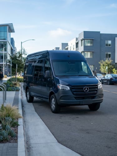 A sharp commercial photograph of a clean, modern dark transport van parked in a structured coastal Playa Vista environment under bright morning daylight, cool blue tones, 35mm.