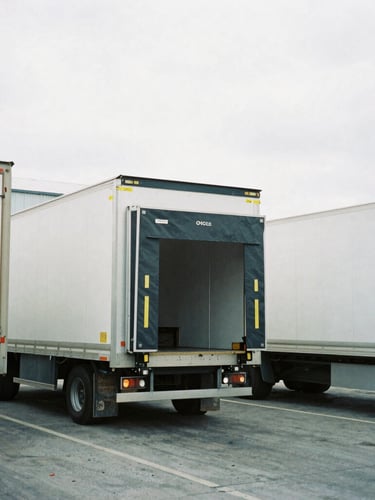 Medium shot of an active industrial loading dock in overcast daylight, clean cargo trailers being loaded, cool desaturated tones, 35mm film
