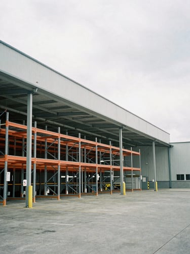 Industrial warehouse interior with high-bay racking and active loading docks under cool overcast daylight, wide-angle environmental framing.