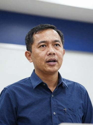Medium close-up of a professional Indonesian lecturer speaking at an academic conference, bright soft indoor lighting, deep blue and white modern background, sharp focus, 35mm lens.