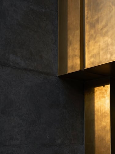 Tight straight-on geometric shot, dramatic high-end interior lighting, dark matte concrete wall meeting brushed brass architectural details.