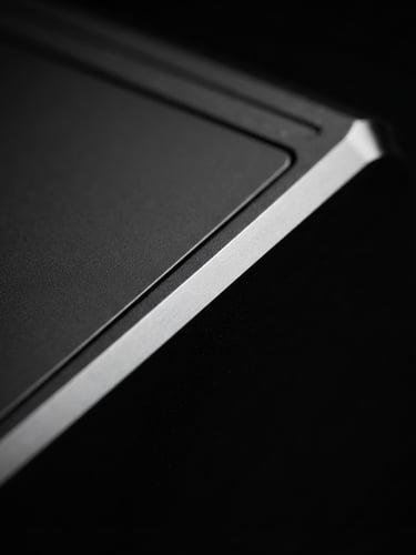 macro close-up of a pristine dark metallic hardware edge, sharp studio lighting, deep shadows, high-contrast monochrome, premium tech photography