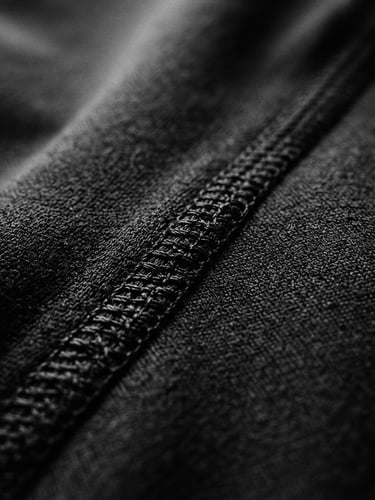 Close-up of technical stitching on raw black athletic fabric, dramatic studio lighting, stark monochrome tones, sharp focus, 35mm film