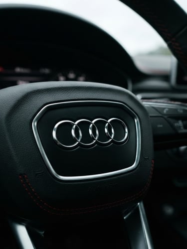 Low-angle close-up of a pristine metallic black Audi steering wheel badge, dramatic overcast daylight, sharp red dashboard stitching details, 35mm lens.