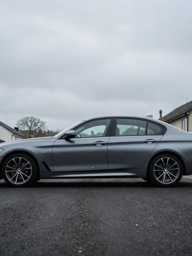 Immaculate side profile of a metallic grey BMW saloon parked in a clean minimalist suburban driveway, moody South Wales overcast sky, 35mm lens.