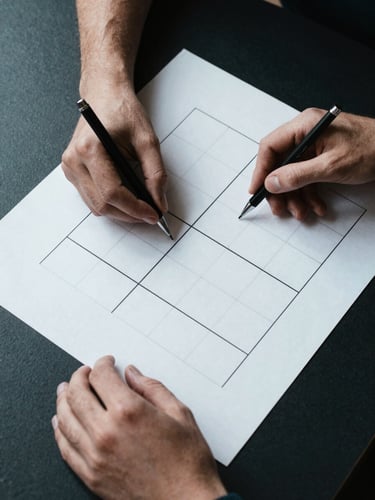 Close overhead flat-lay of a designer's hands placing a printed wireframe grid on a dark desk, a mechanical pencil resting at the edge, studio strobe lighting emphasising teal and white contrast, tight crop with strong shadow geometry