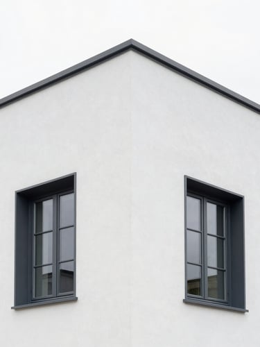 A pristine exterior house facade with sharp corners finished in clean white crépi, contrasting with dark grey window frames under soft Belgian daylight.