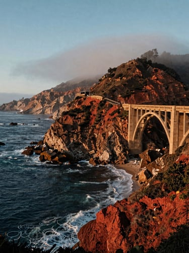 Cinematic wide shot of the Bixby Creek Bridge on the California coast, dramatic cliffs plunging into the deep blue Pacific Ocean, soft coastal fog, warm evening light.
