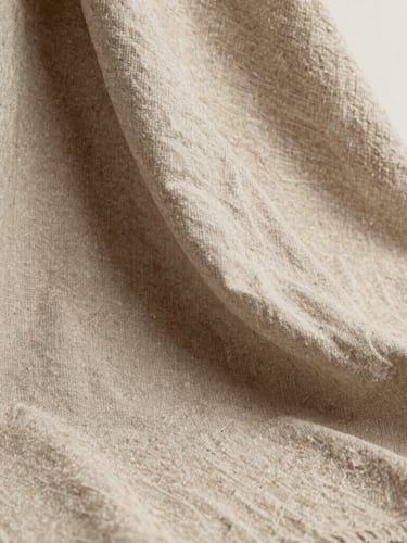 Close-up of high-quality textured beige linen fabric draped elegantly, soft natural daylight casting gentle shadows, editorial fashion photography style, neutral sand tones, 35mm