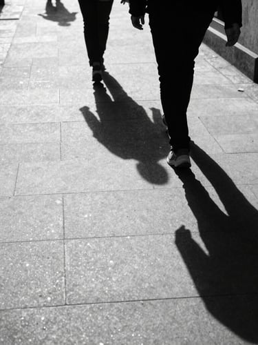 High-contrast street scene in London, harsh direct sunlight casting long deep shadows across concrete, a solitary figure walking, gritty 35mm tri-x film grain.