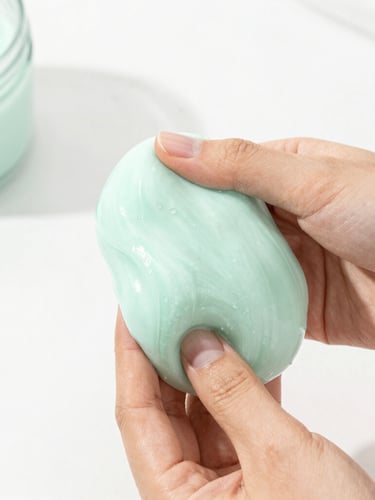 Bright high-key product photography of hands squishing pastel mint textured slime, soft natural daylight, clean minimalist styling