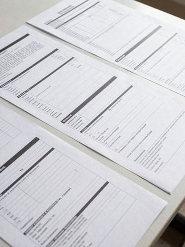 Overhead close-up of organized construction documents, inspection checklists, and plan sets laid flat on a clean work surface under bright even studio light, no people visible, order and precision evident