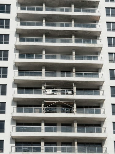 Wide environmental shot of a South Florida condominium building facade under bright even daylight, structural inspection points and exposed concrete balcony edges visible, scaffolding framing the mid-section, no people, precise and legible
