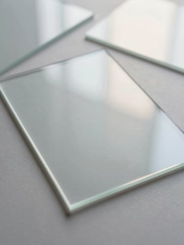 Overhead flat lay of translucent glass sheets reflecting soft morning light, pearlescent paper mockups, silver gray tones, serene empty space